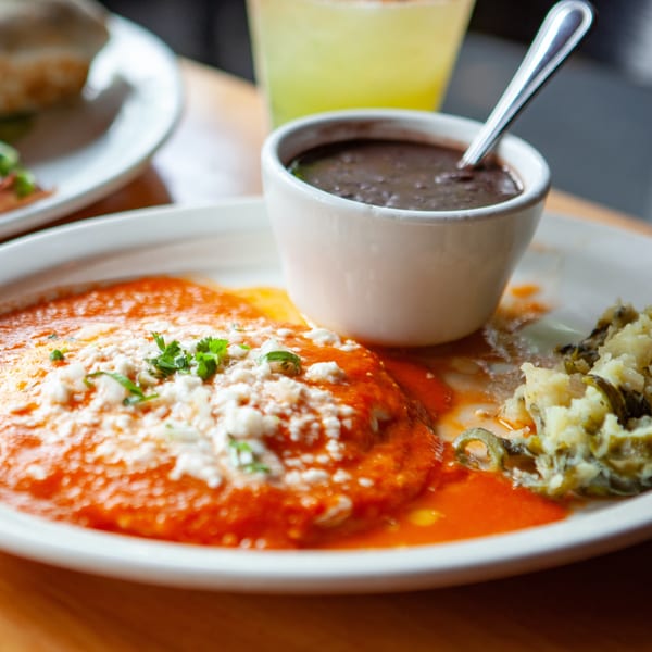 Mexican dish with red sauce, crumbled cheese, black beans, and mashed potatoes on a white plate.