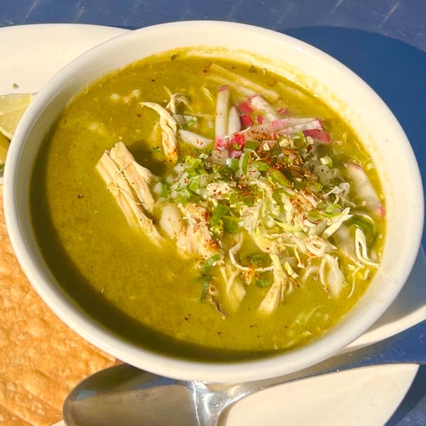 A white bowl of Loteria Grill's green pozole with shredded chicken, radishes, and cilantro.