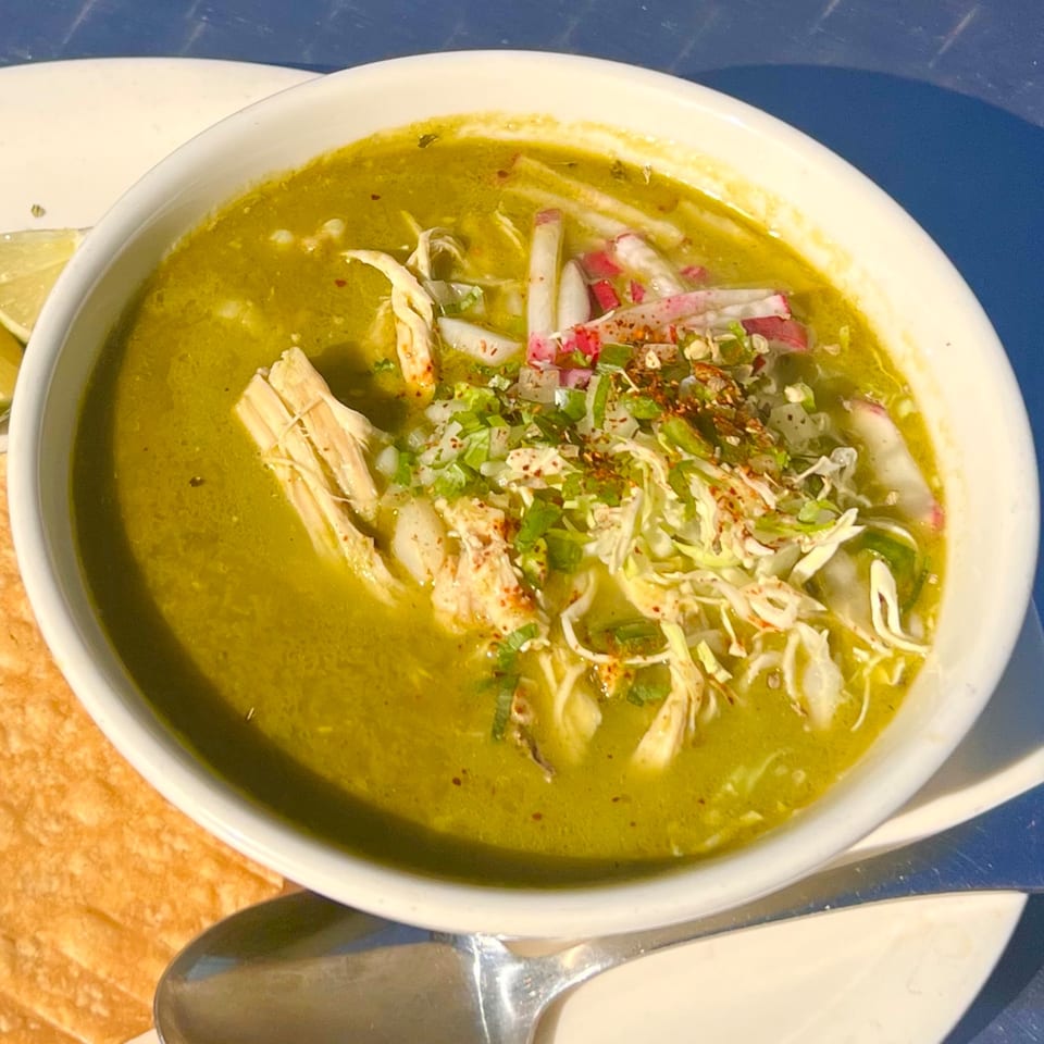 A white bowl of Loteria Grill's green pozole with shredded chicken, radishes, and cilantro.
