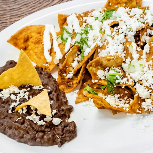 Chilaquiles with black beans, topped with cheese, sour cream, and cilantro on a white plate.