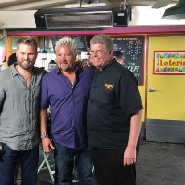 Three men, including Guy Fieri, pose together inside Loteria Grill, a Mexican restaurant.