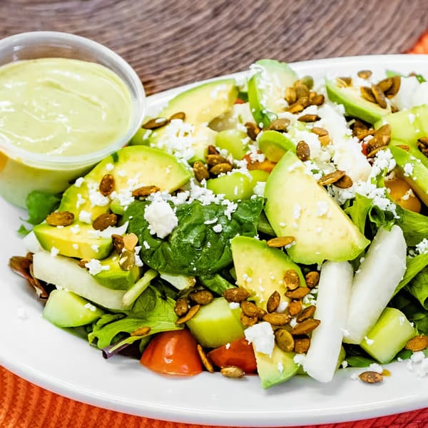 Loteria Grill's avocado salad with greens, tomatoes, cheese, pumpkin seeds, and a side of dressing.